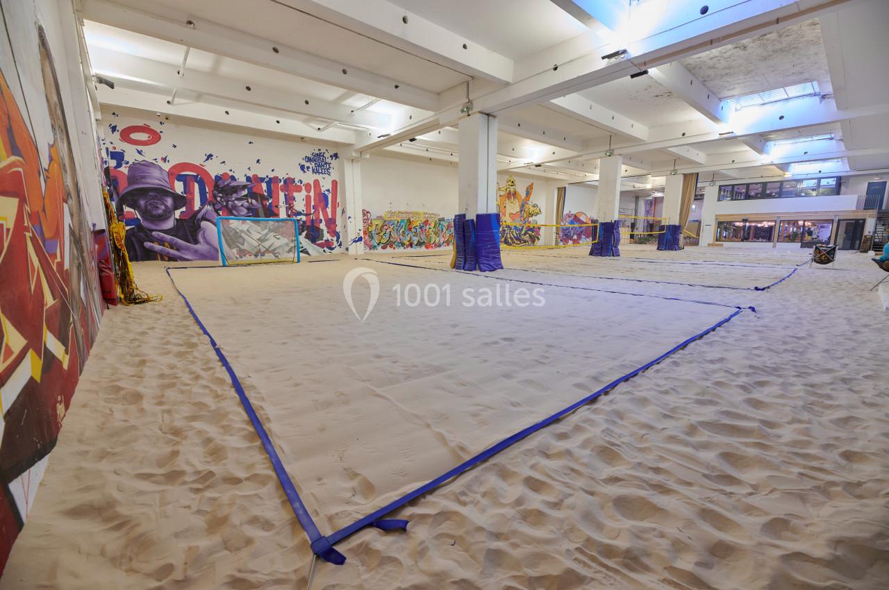 Terrain de sable intérieur délimité par des lignes bleues, entouré de murs décorés de graffitis colorés.