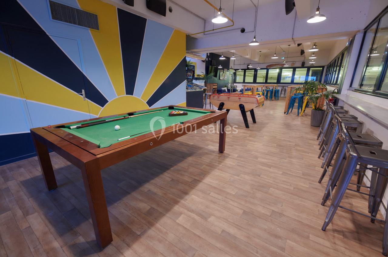 Salle de détente avec une table de billard, un baby-foot, des tabourets hauts et un décor coloré.