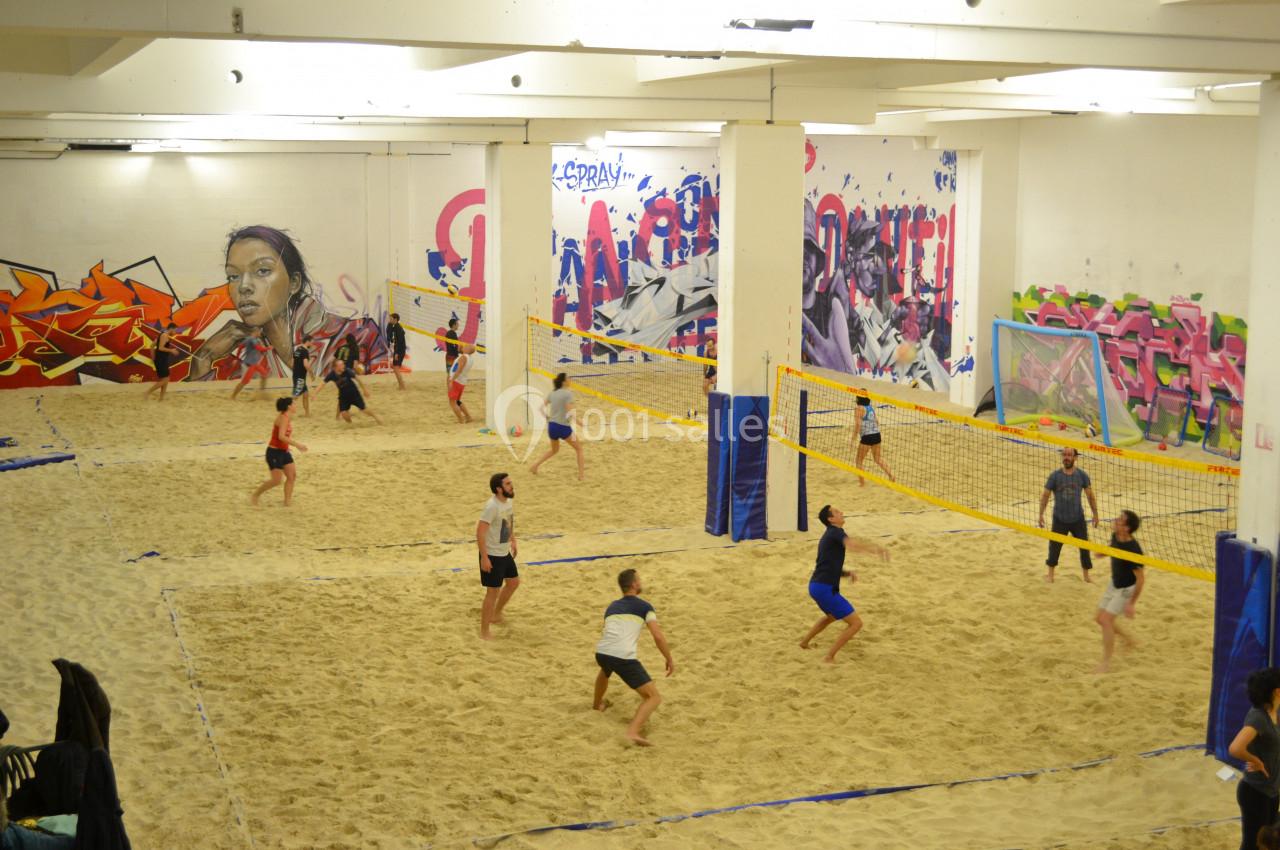Des personnes jouent au beach-volley sur du sable dans un gymnase décoré de graffitis colorés.
