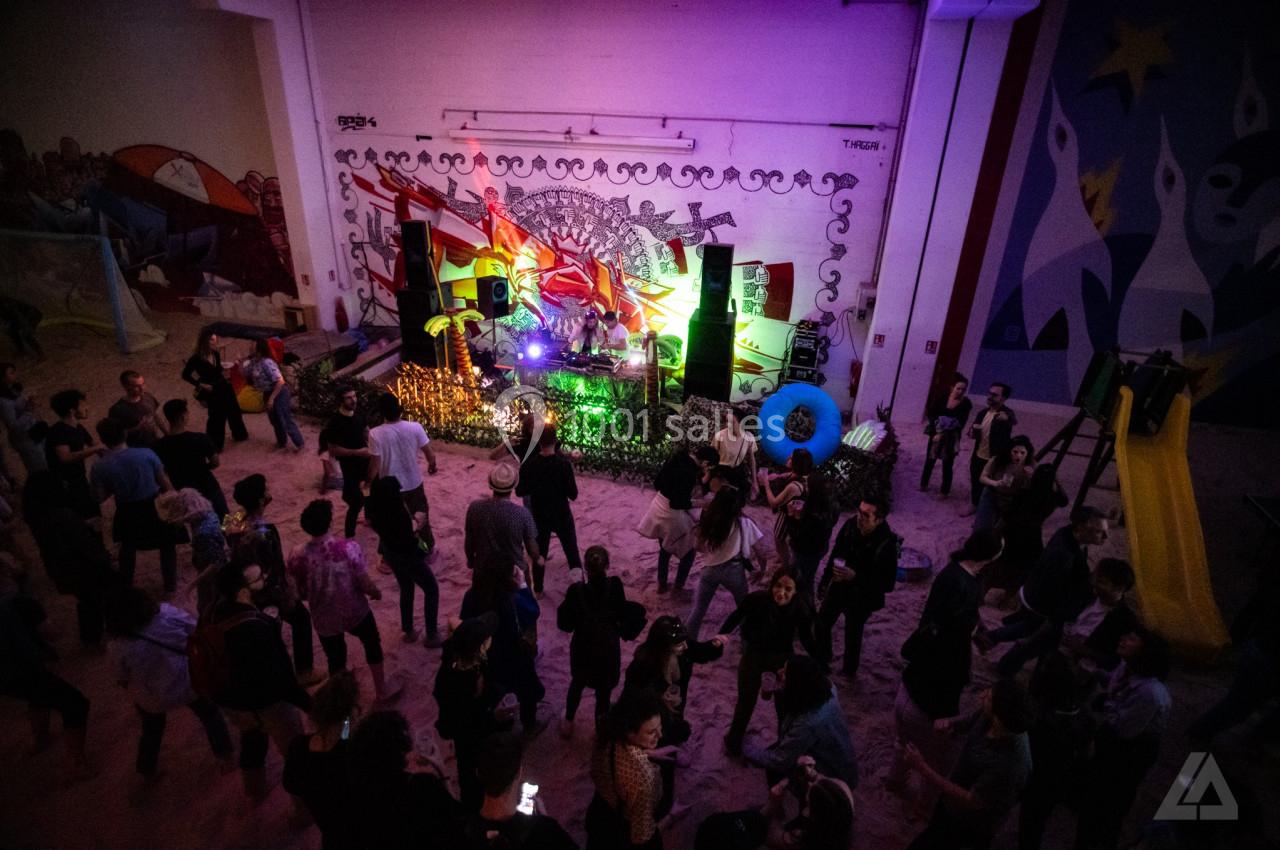 Groupe de personnes dans une salle colorée avec un DJ sur une scène décorée et des graffitis en arrière-plan.