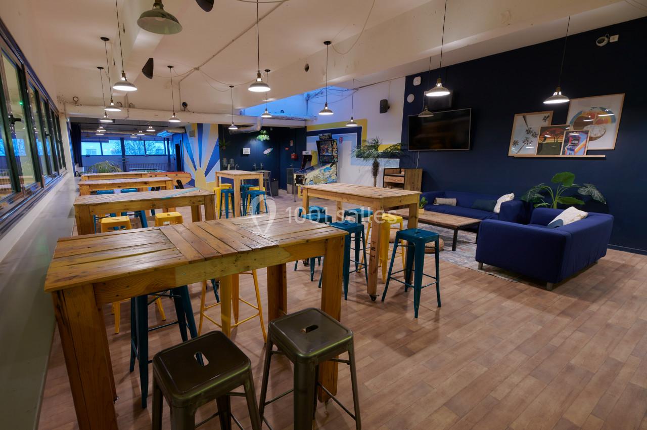 Salle conviviale avec tables en bois, tabourets colorés, canapé bleu et décorations murales modernes.