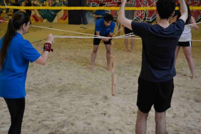Des personnes participent à un jeu d'adresse avec des labyrinthes en bois dans un espace intérieur sur sol sablé.