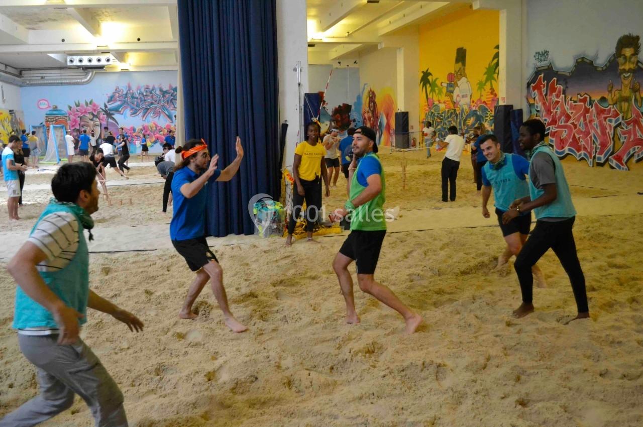 Des personnes jouent au volley-ball sur un terrain de sable en intérieur, entourées de graffitis colorés.