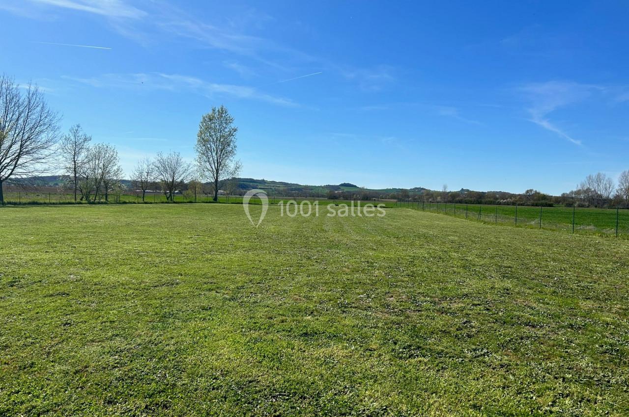 Champ verdoyant sous un ciel bleu dégagé, bordé d'arbres et de collines à l'horizon.
