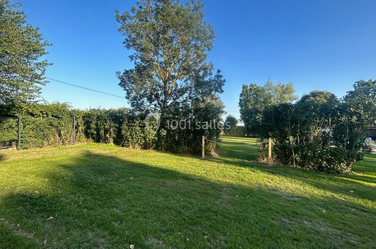 Pelouse verdoyante bordée de haies et d'arbres sous un ciel bleu dégagé.