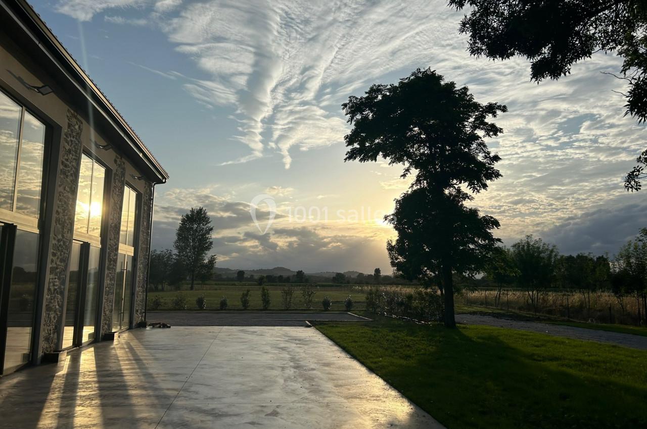 Coucher de soleil illuminant une terrasse en béton, avec un arbre et un paysage champêtre en arrière-plan.