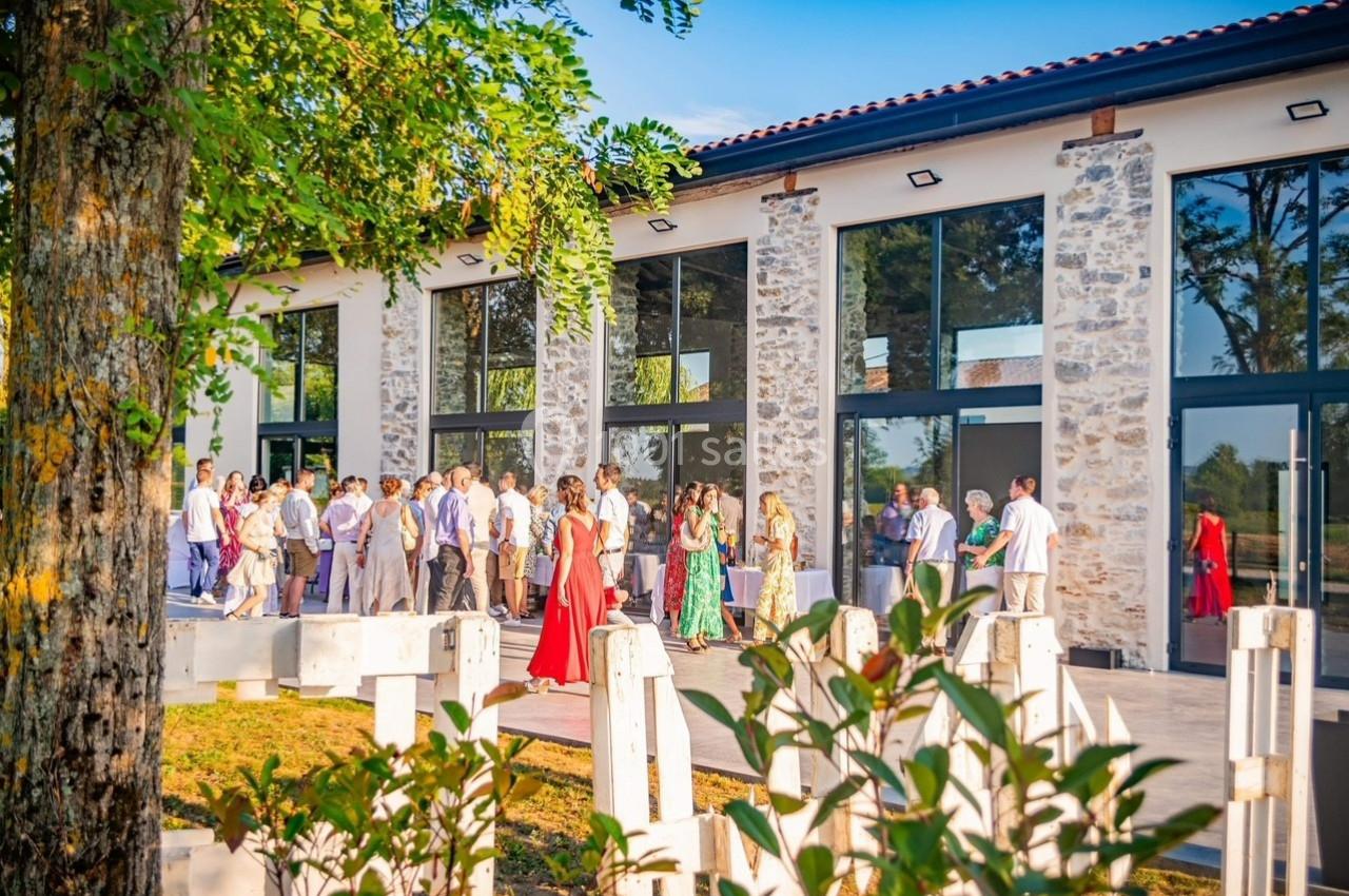 Groupe de personnes rassemblées devant un bâtiment moderne en pierre, lors d'un événement en plein air par temps ensoleillé.