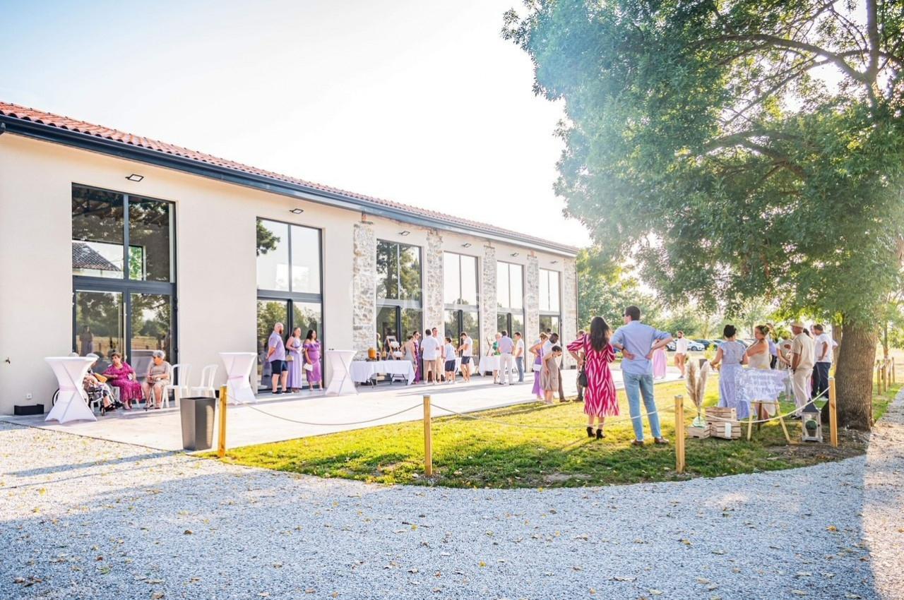 Groupe de personnes rassemblées devant un bâtiment moderne avec de grandes baies vitrées, par une journée ensoleillée.