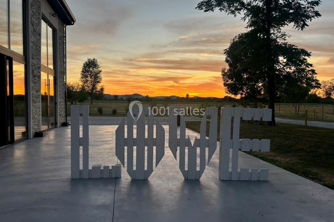 Lettres blanches formant le mot ’LOVE’ sur une terrasse au coucher du soleil avec des arbres et un paysage en arrière-plan.