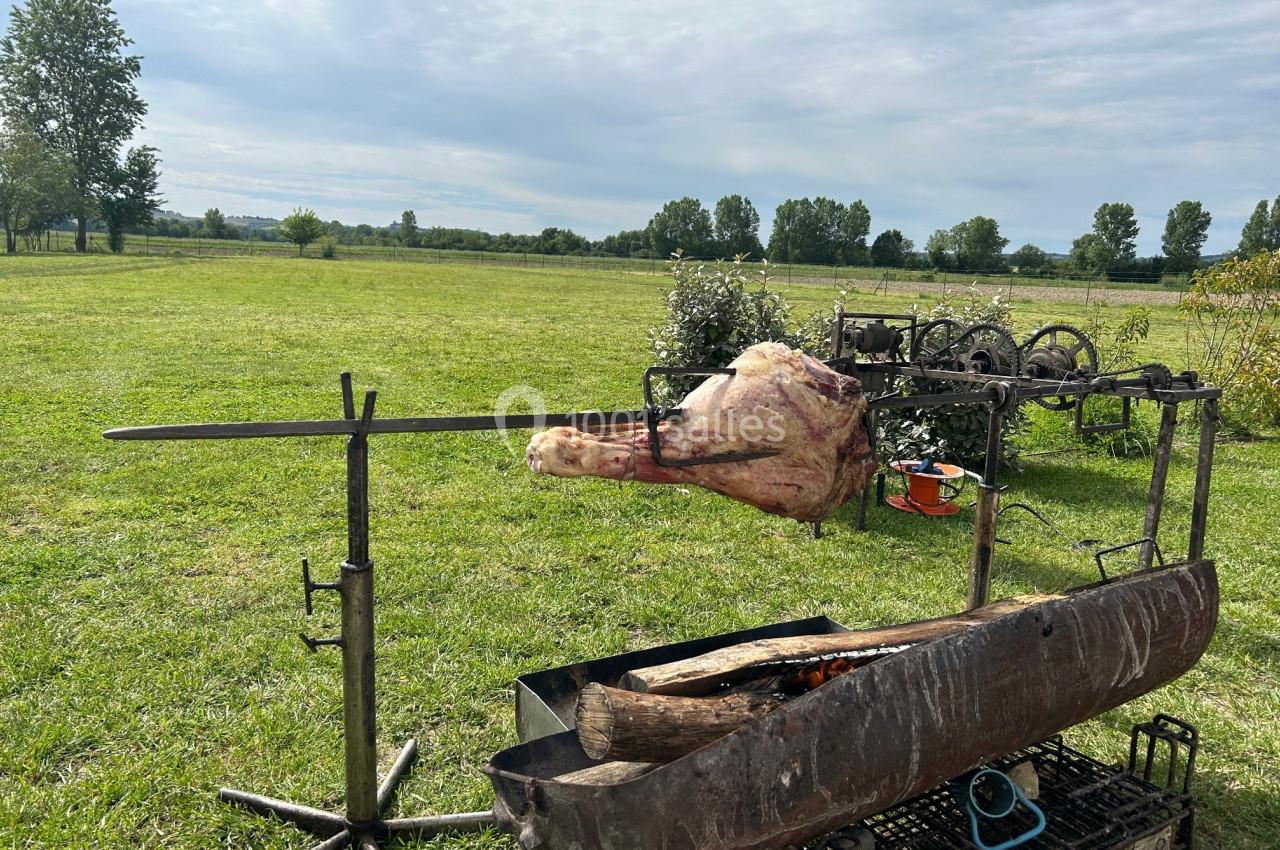 Un morceau de viande cuit à la broche au-dessus d'un feu de bois dans un champ verdoyant.