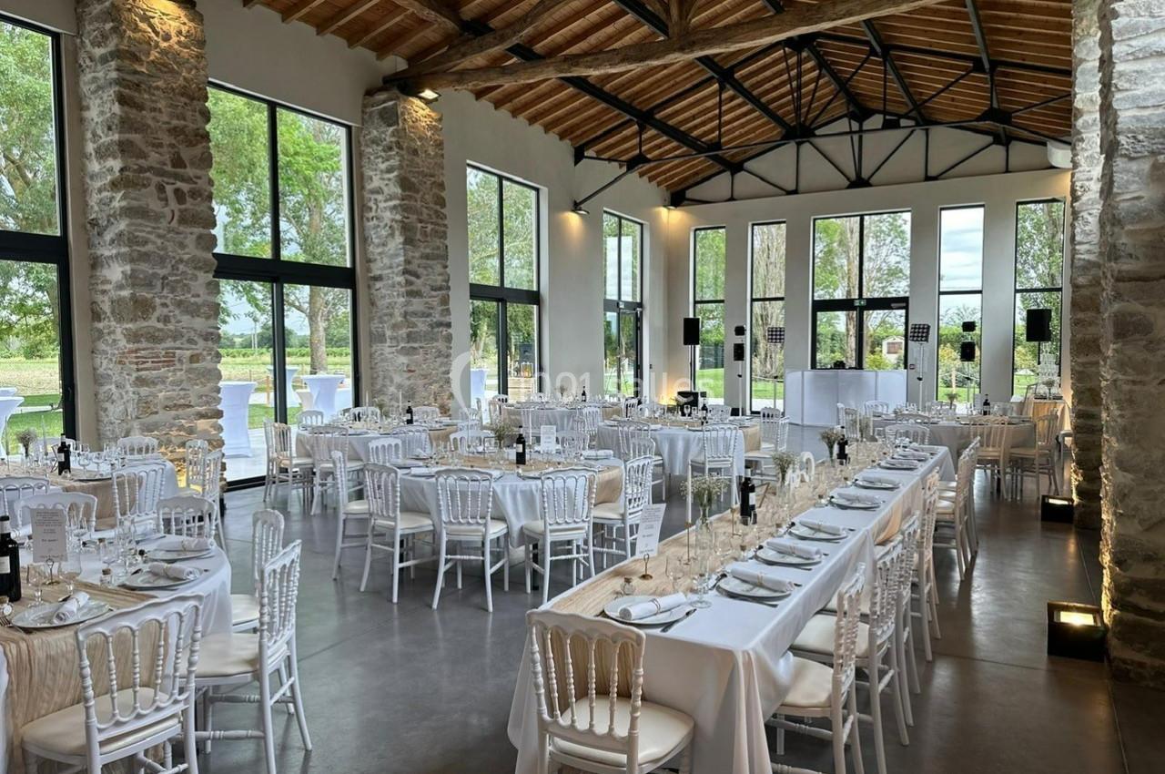 Salle de réception lumineuse avec murs en pierre, grandes baies vitrées et tables dressées pour un événement.