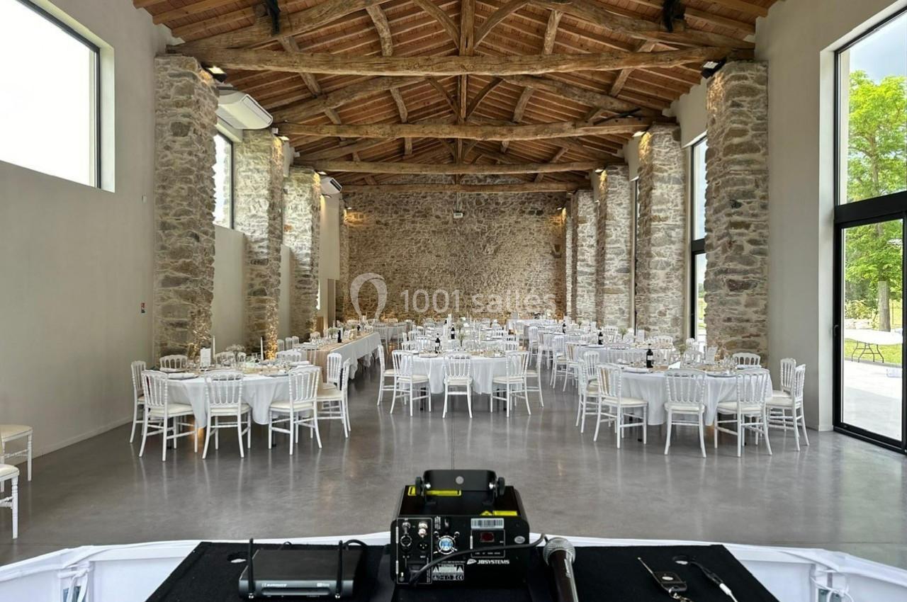 Salle de réception en pierre avec tables rondes dressées et vue depuis une scène équipée de matériel audio.