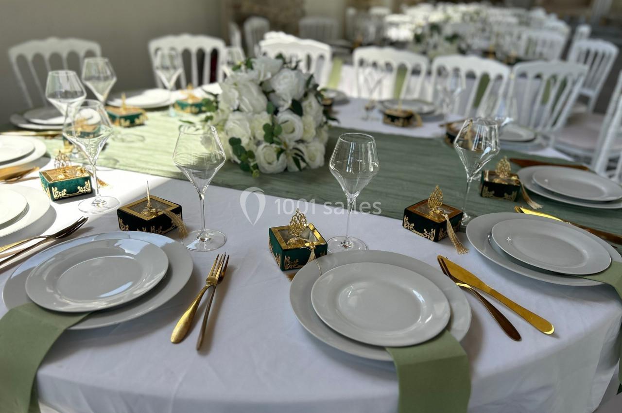 Table de réception élégamment dressée avec nappes blanches, couverts dorés, serviettes vertes et centre de table floral.