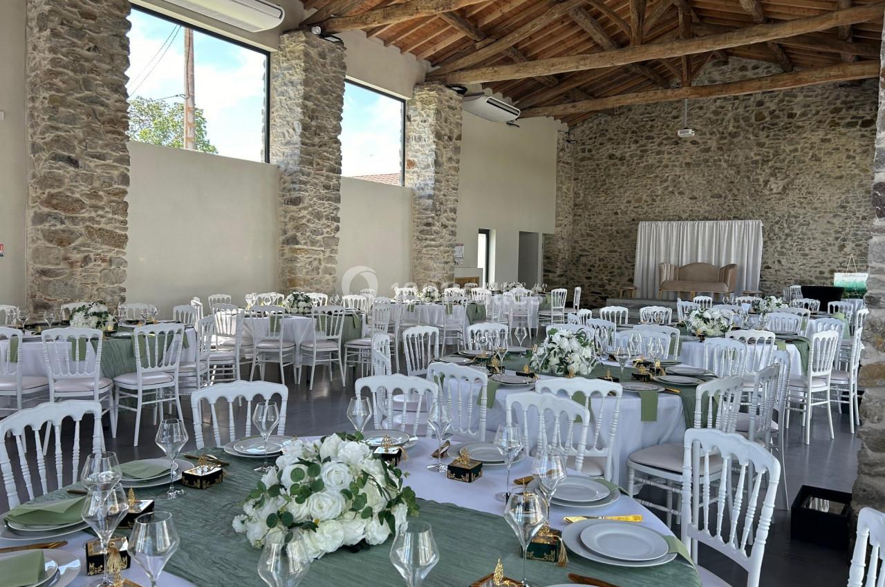 Salle de réception décorée pour un événement, avec tables dressées, nappes vertes et arrangements floraux blancs.