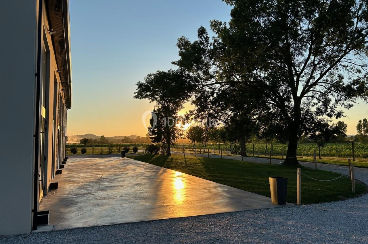 Allée en béton réfléchissant la lumière du coucher de soleil, bordée d'arbres et de pelouses verdoyantes.