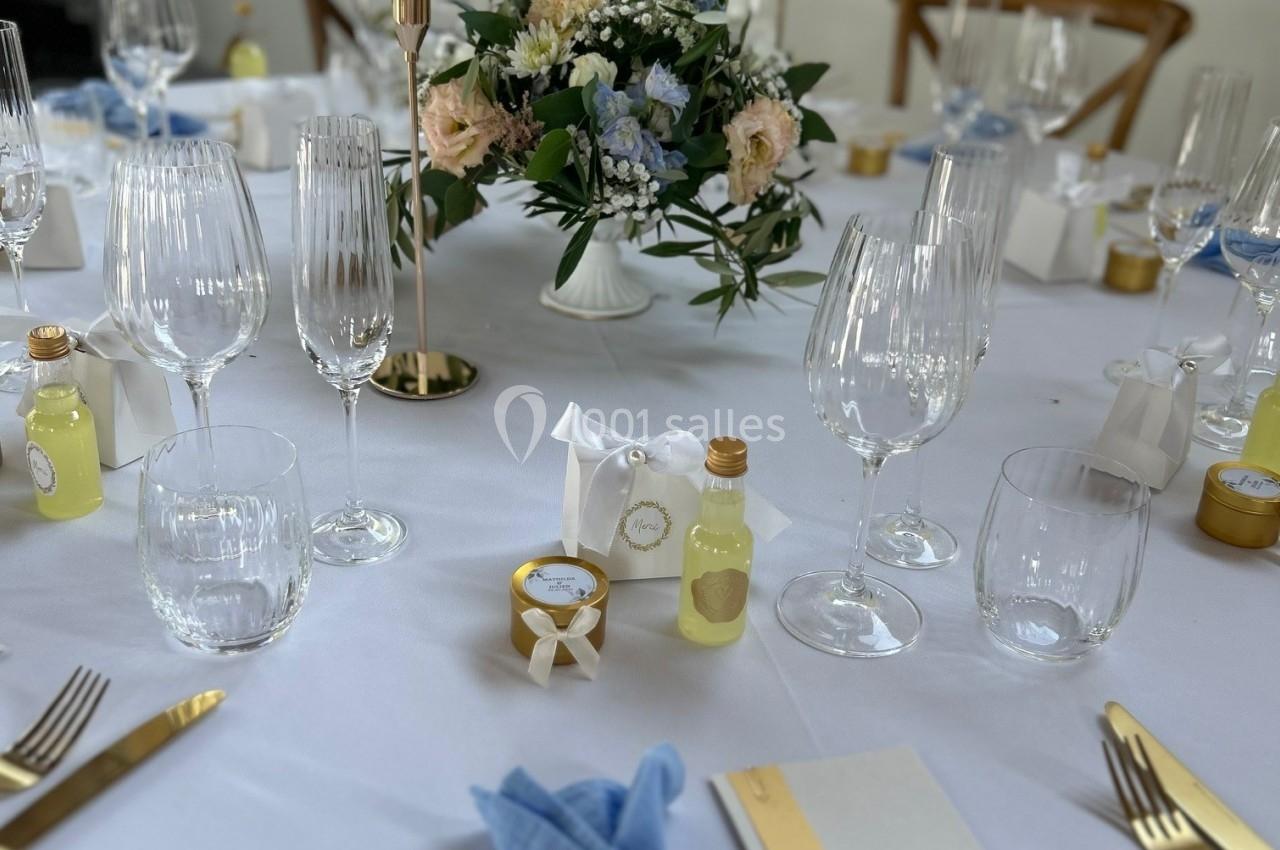 Table élégamment dressée avec des couverts dorés, serviettes bleues, bougies, fleurs et menus pour un repas formel.