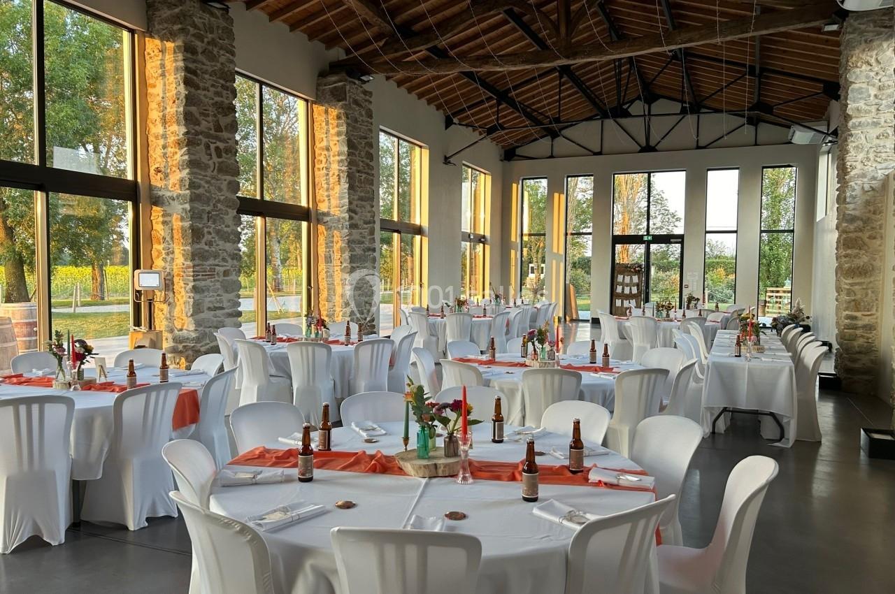 Salle de réception lumineuse avec des tables rondes dressées, nappes blanches et décorations florales.
