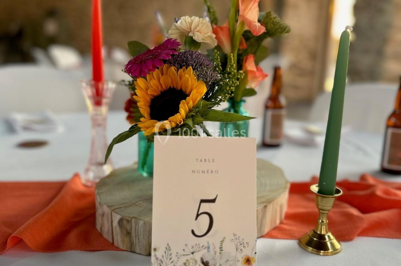 Centre de table avec fleurs colorées, bougies rouge et verte, et une carte indiquant ’Table numéro 5’.