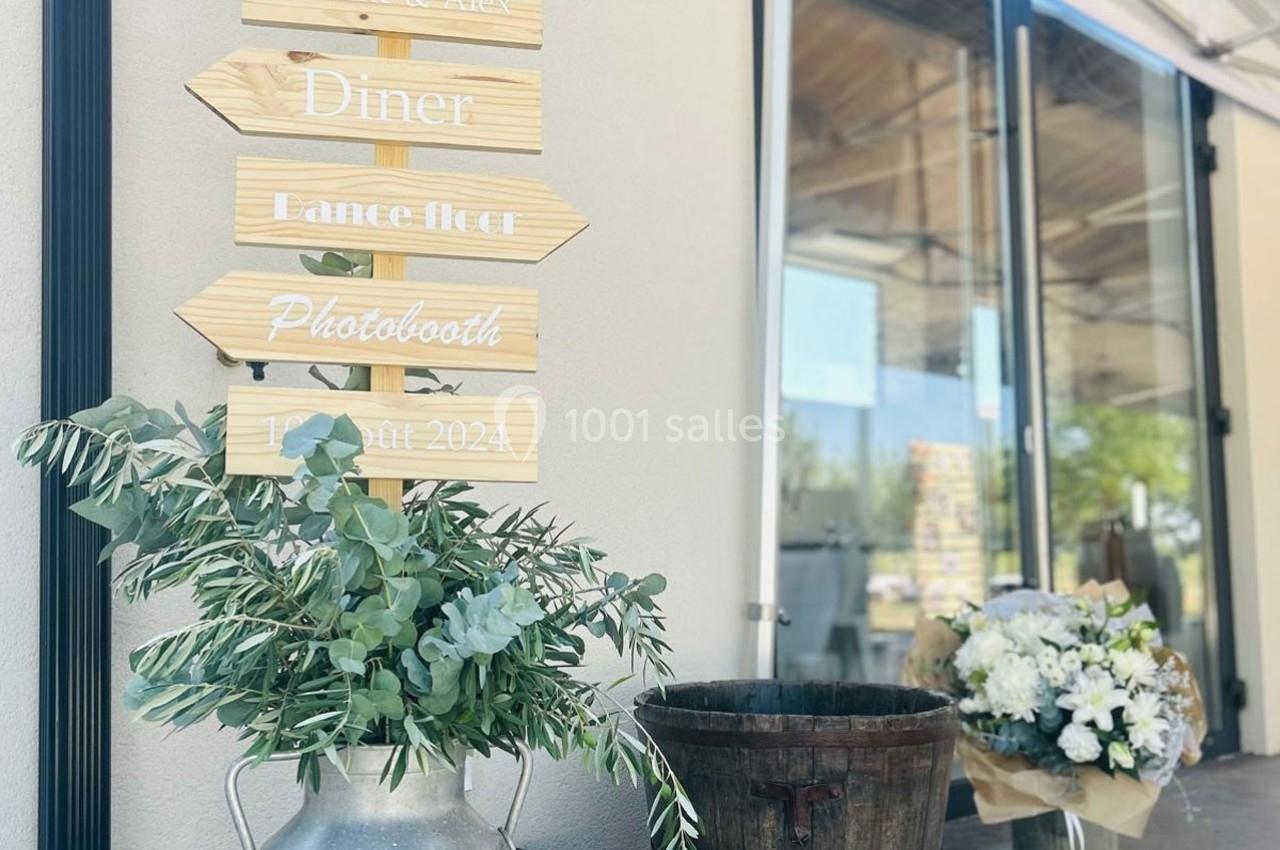 Panneau en bois indiquant des activités, entouré de feuillage, d'un seau en bois et d'un bouquet de fleurs blanches.