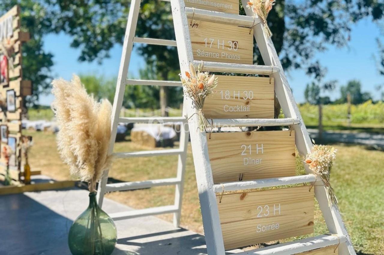 Échelle en bois décorée avec des fleurs séchées, affichant un programme d'événements en plein air par une journée…