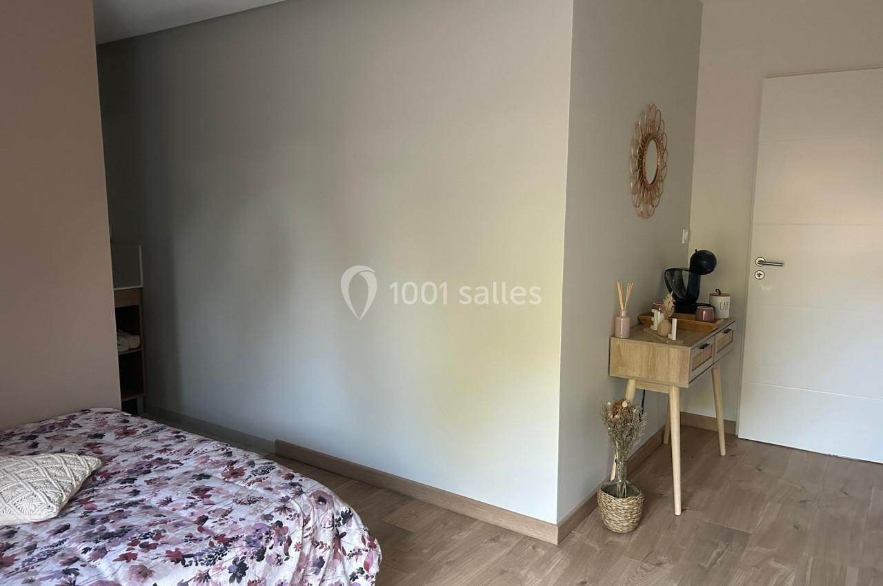 Chambre lumineuse avec lit à motif floral, mur beige, console en bois clair et décoration minimaliste.