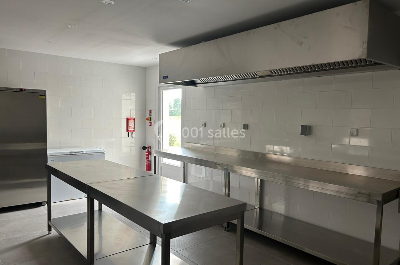 Cuisine professionnelle avec plans de travail en inox, hotte d'extraction, réfrigérateur et murs carrelés blancs.