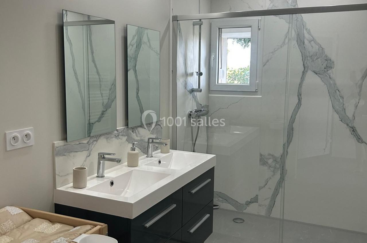 Salle de bain moderne avec double vasque, miroirs, douche à l'italienne et murs en carrelage effet marbre.