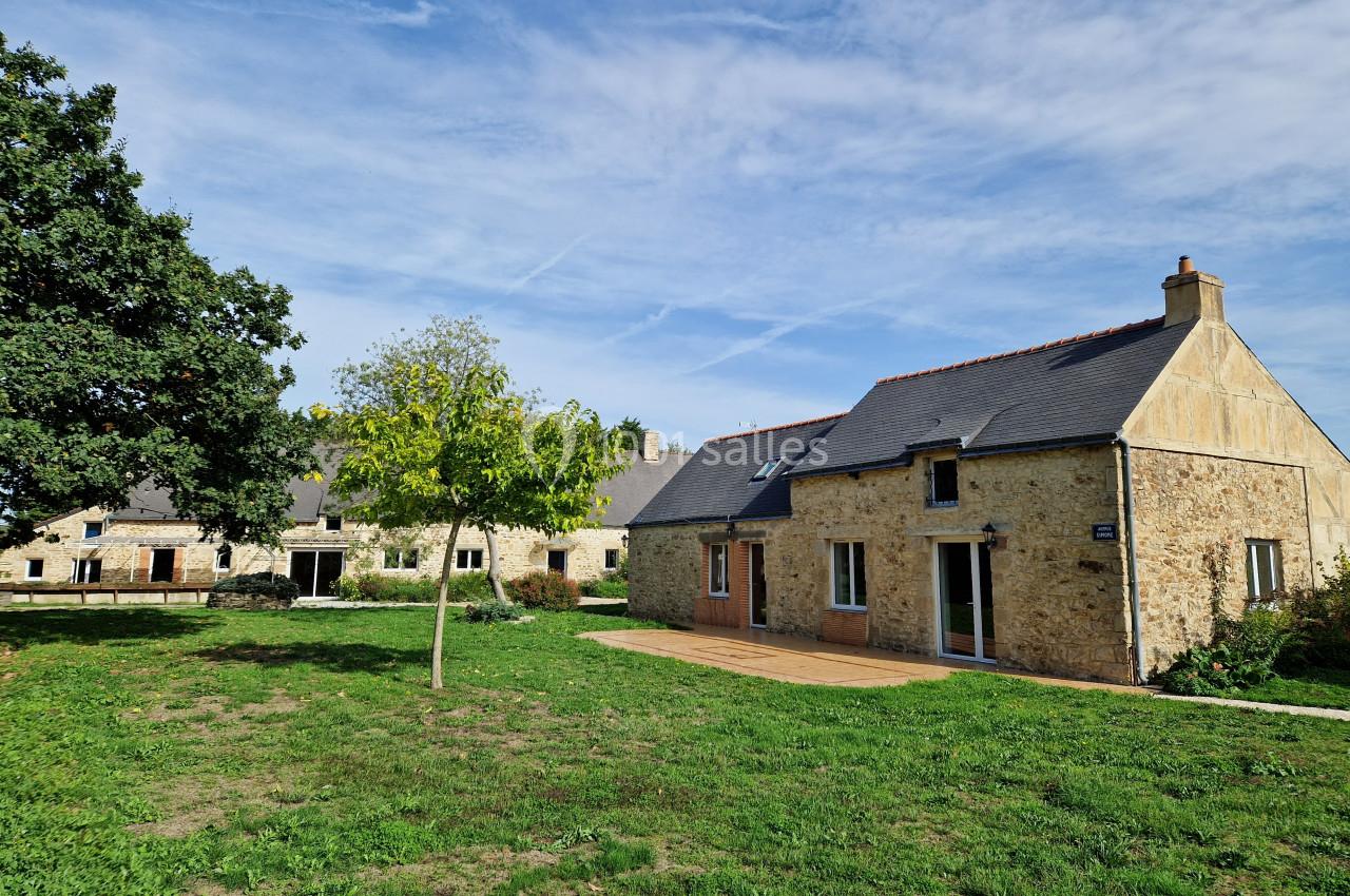 Bâtiments en pierre avec toits en ardoise entourés de pelouse et d'arbres sous un ciel bleu.