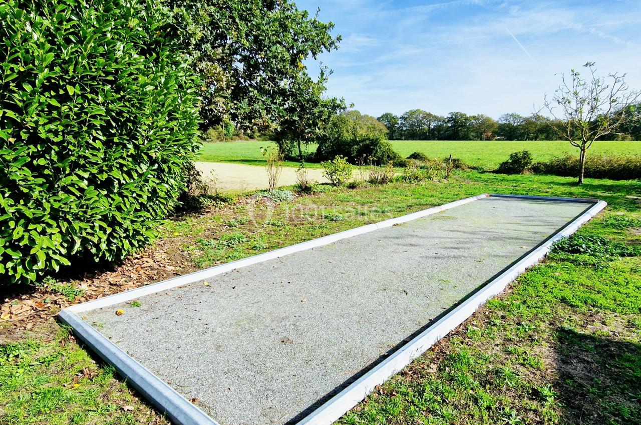 Terrain de pétanque en gravier entouré de verdure, situé dans un espace extérieur ensoleillé.