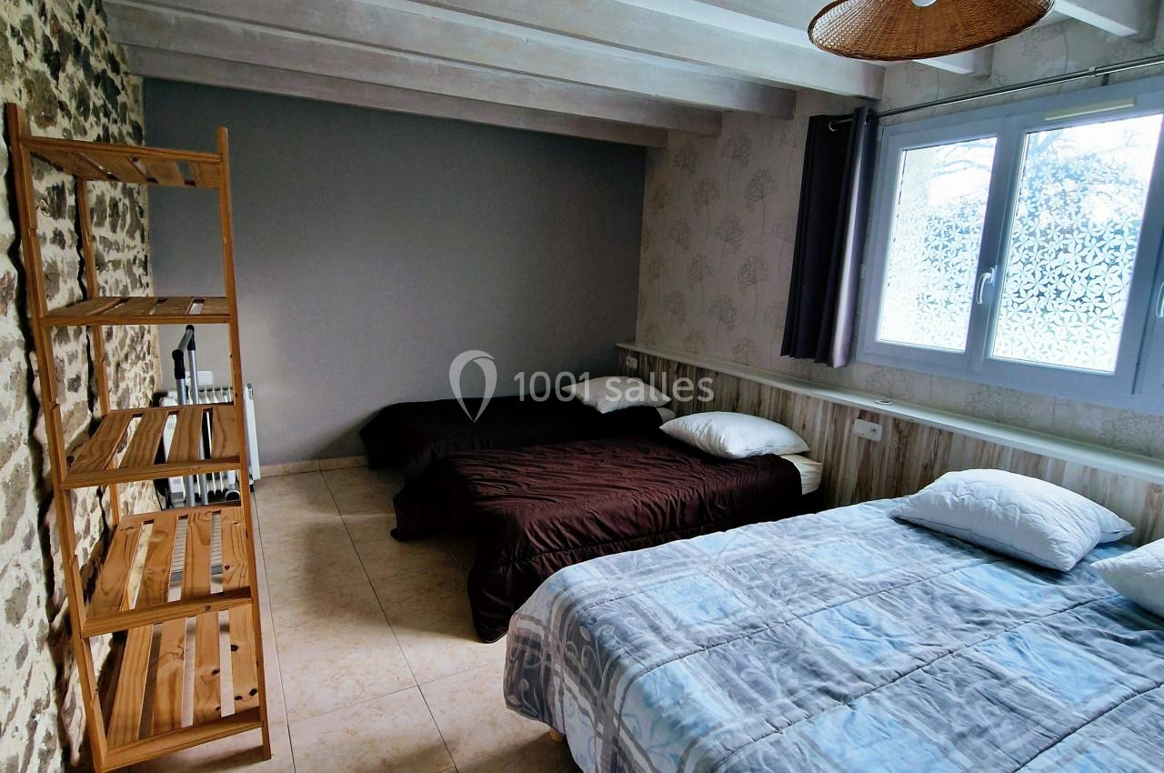 Chambre avec deux lits doubles, étagère en bois, mur en pierre et grande fenêtre laissant entrer la lumière naturelle.