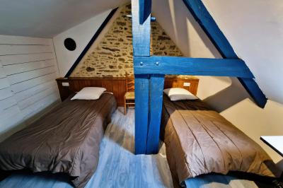 Deux lits avec couvertures bleues et marron dans une chambre lumineuse au sol en parquet et mur clair.