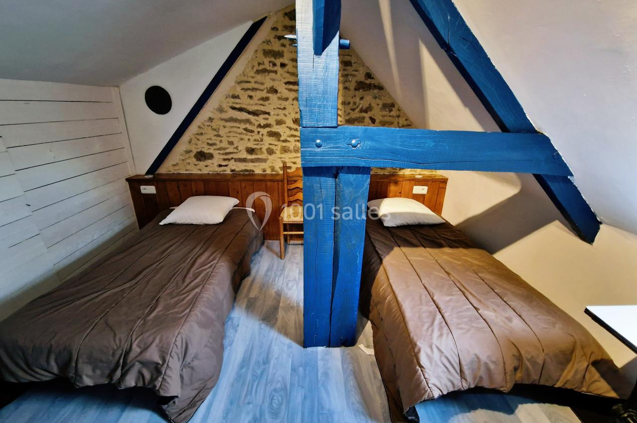 Deux lits simples avec couettes marron dans une chambre mansardée aux poutres apparentes et mur en pierre.