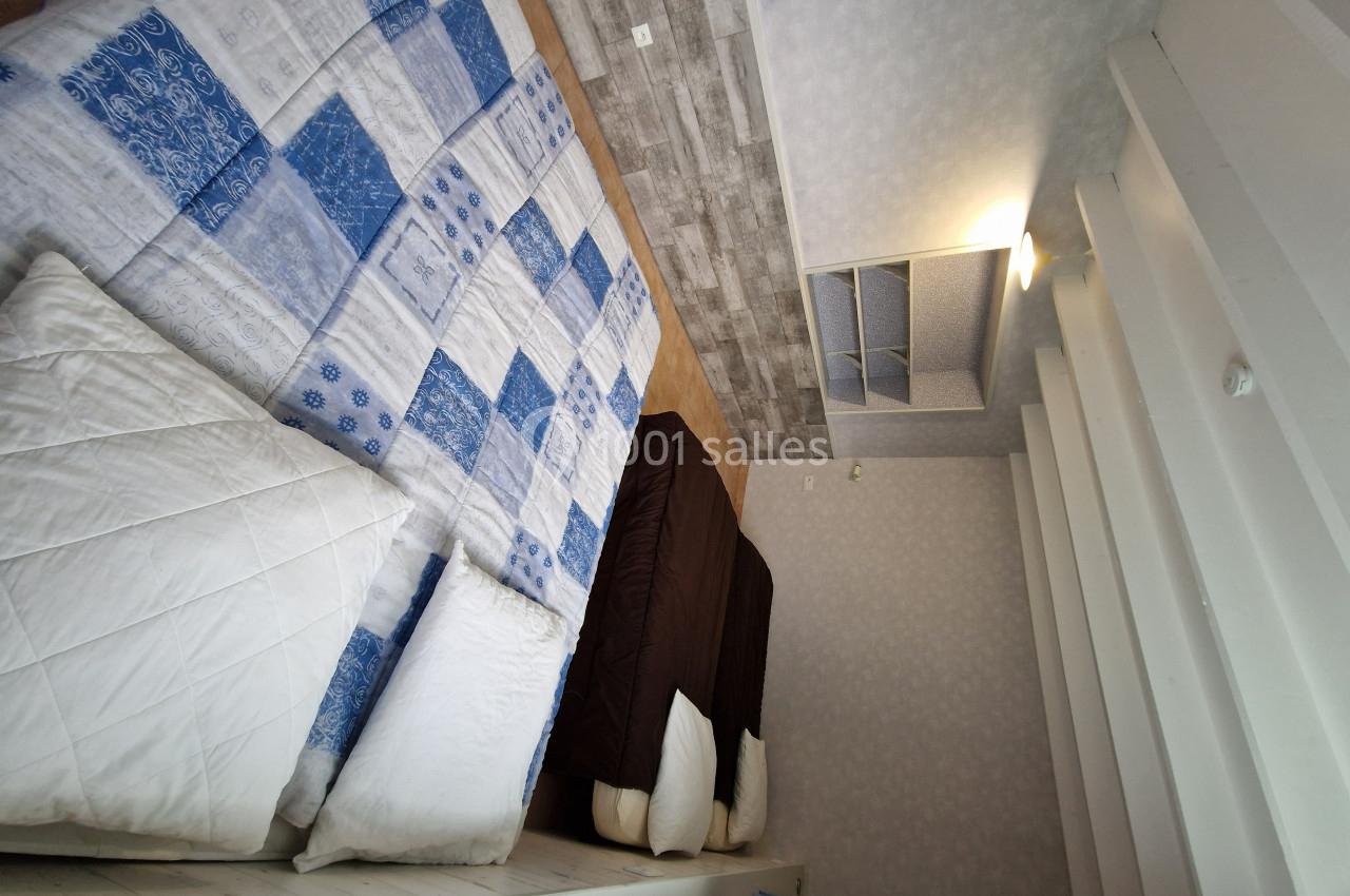 Deux lits avec couvertures bleues et marron dans une chambre lumineuse au sol en parquet et mur clair.