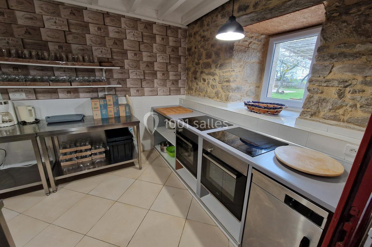 Cuisine équipée avec plan de travail, plaques de cuisson, four, étagères métalliques et fenêtre donnant sur un jardin.