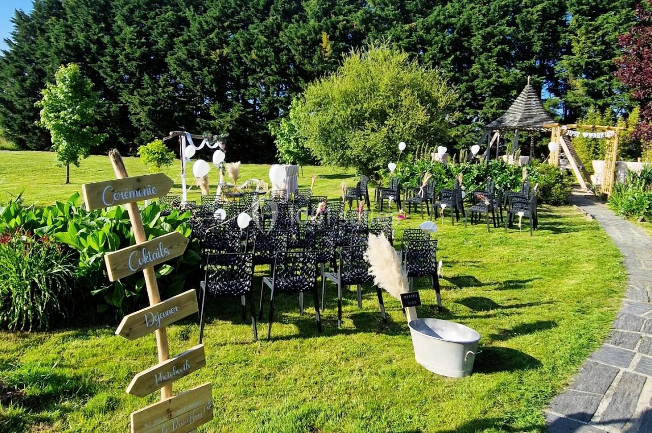 Chaises noires alignées en extérieur pour une cérémonie, avec panneaux directionnels et décorations sur une pelouse…