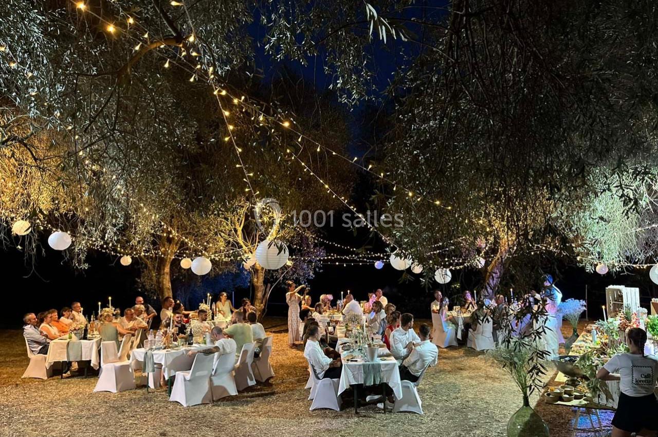 Dîner en plein air sous des guirlandes lumineuses et lanternes, avec des invités assis à des tables décorées.