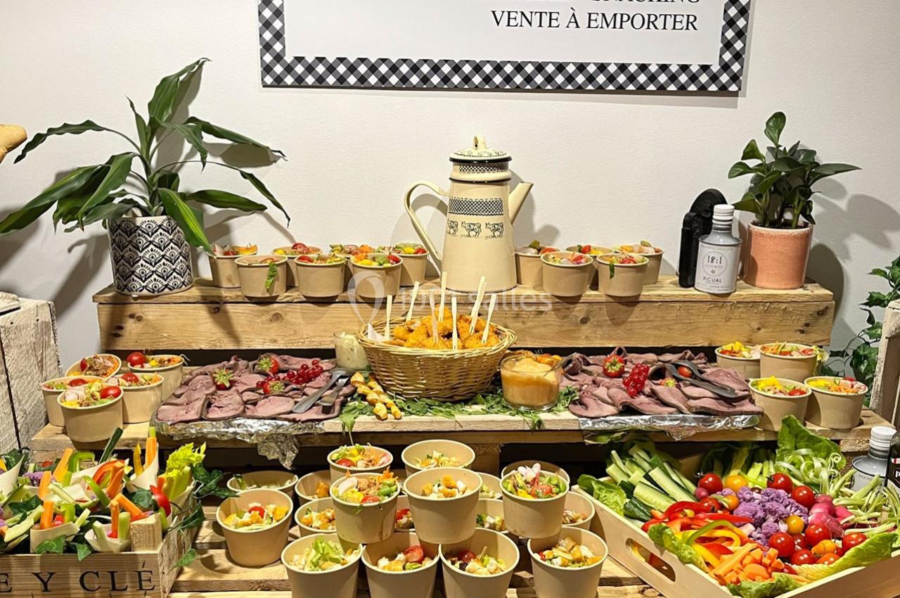 Buffet composé de salades, légumes frais, viandes froides et condiments, présenté sur une table en bois.