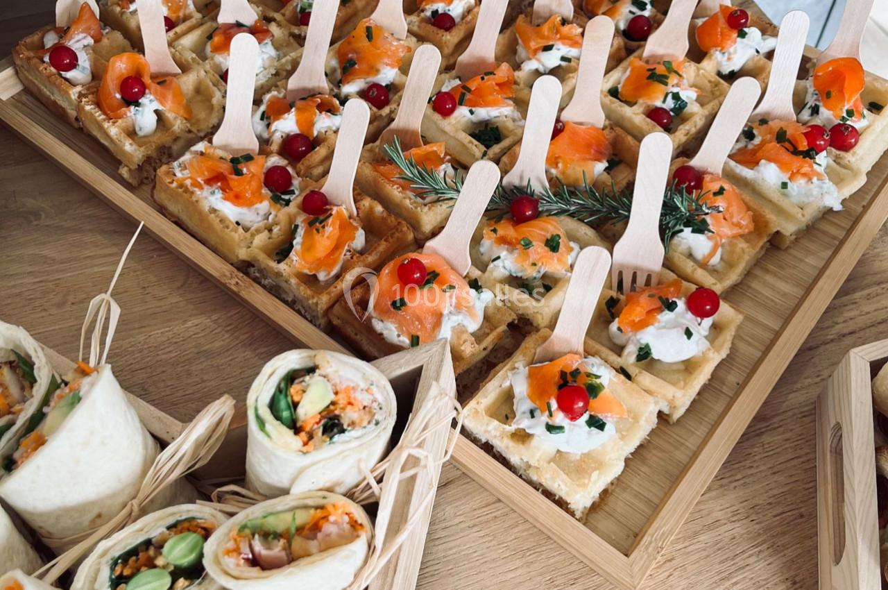 Plateau de bouchées apéritives comprenant wraps garnis et gaufres salées au saumon et fromage frais, décorées de baies…