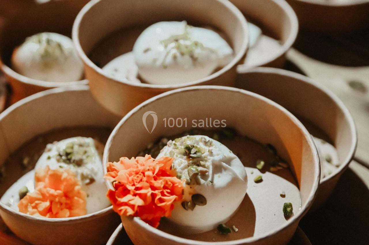 Desserts blancs garnis de pistaches et fleurs orange, présentés dans des bols en carton.