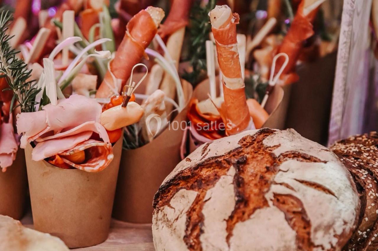 Assortiment de charcuteries et légumes en verrines avec un pain artisanal en premier plan.
