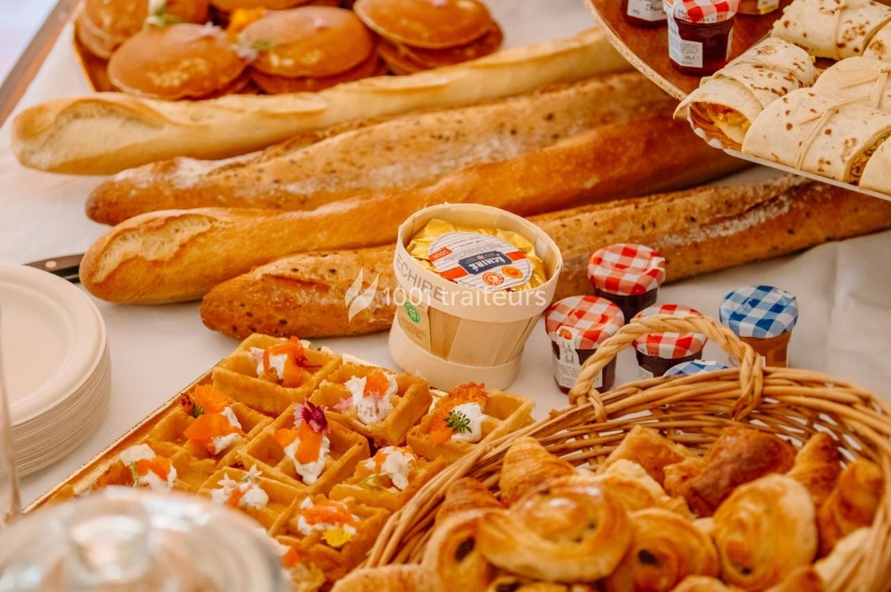 Assortiment de viennoiseries, baguettes, gaufres garnies et confitures sur une table.