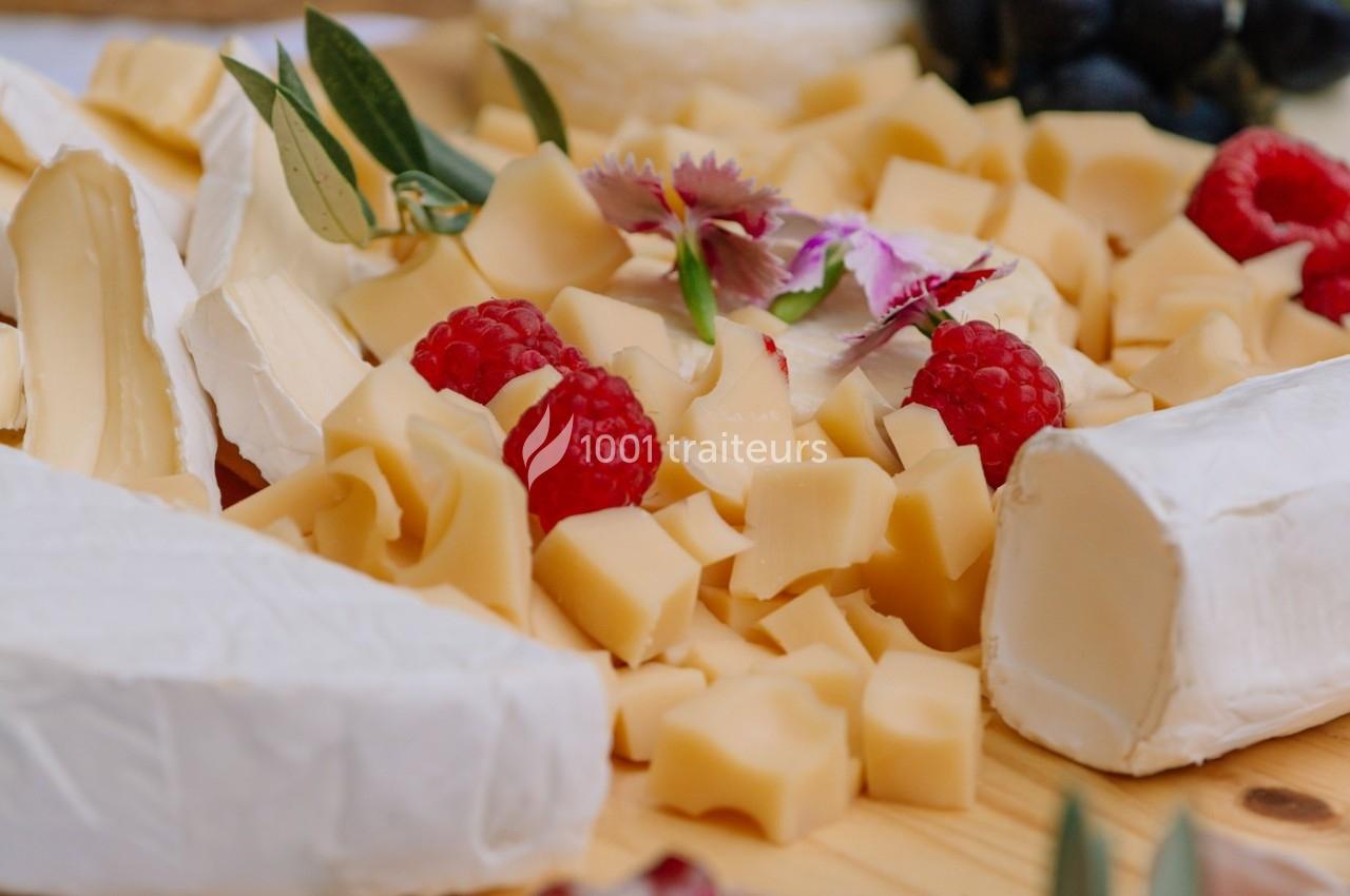 Assortiment de fromages variés avec framboises, fleurs décoratives et olives sur une planche en bois.