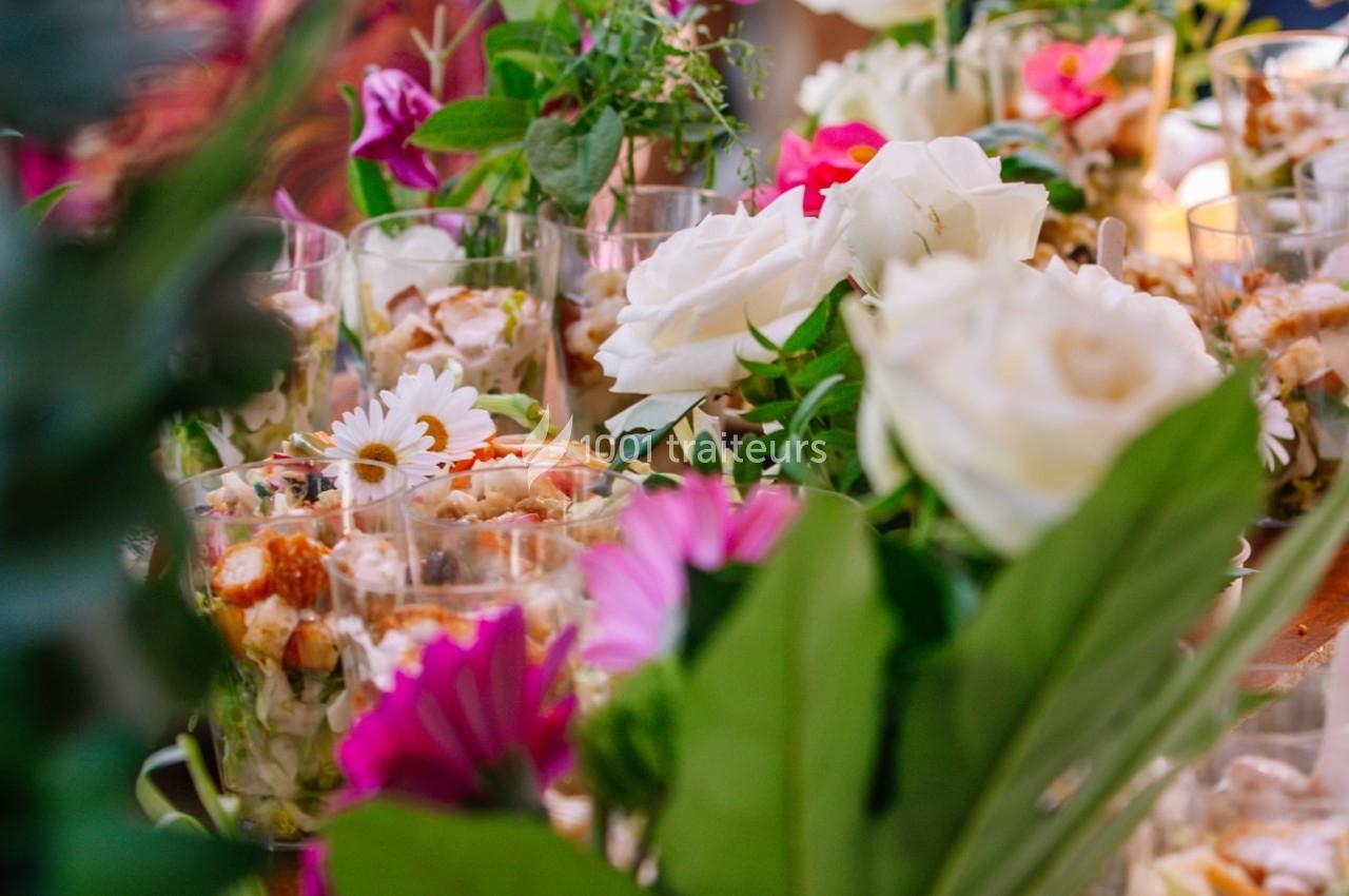 Arrangement de fleurs blanches et roses entourant des verrines garnies, dans un décor lumineux et coloré.