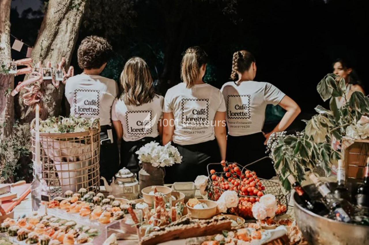 Quatre personnes de dos portant des t-shirts assortis, devant une table garnie de plats et boissons en extérieur.