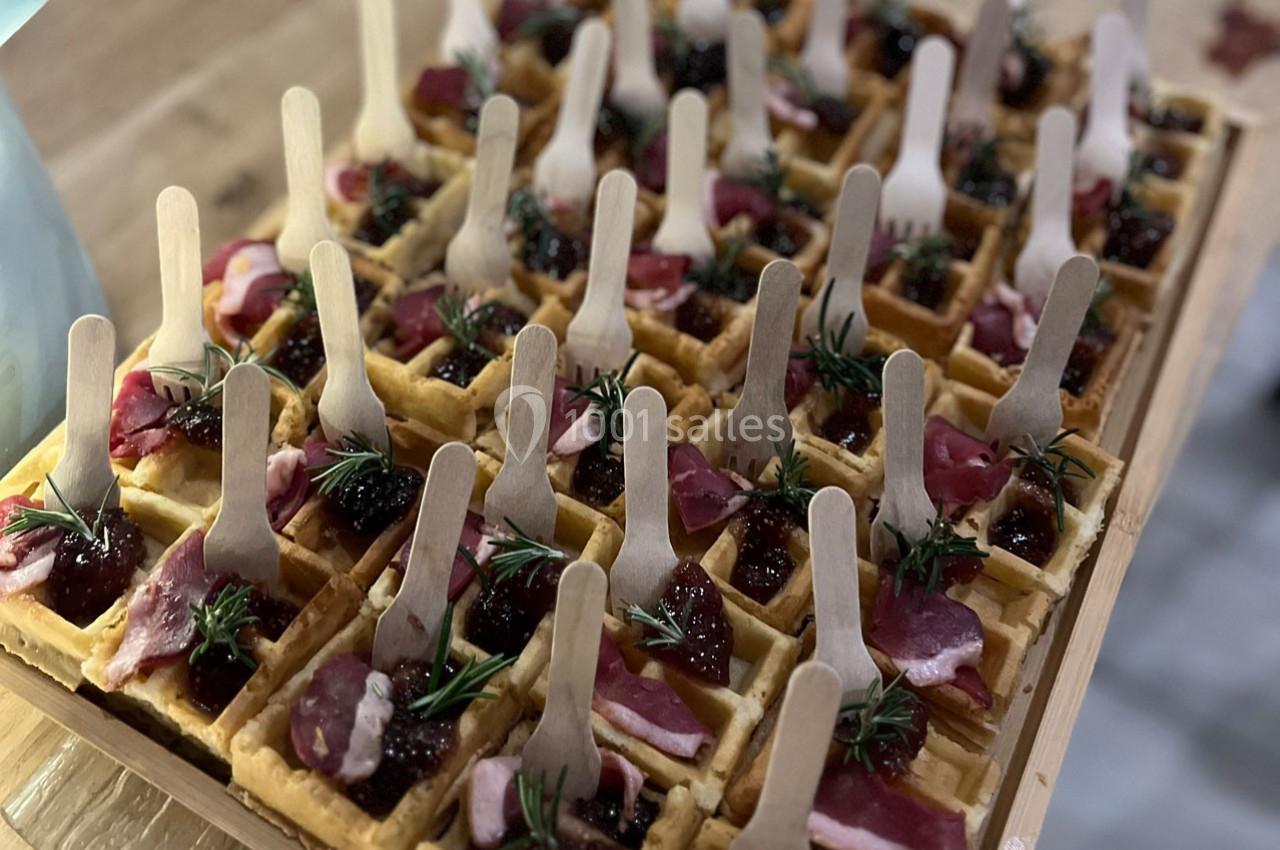 Plateau de mini-gaufres garnies de viande séchée, confiture et brins de romarin, avec des fourchettes en bois.