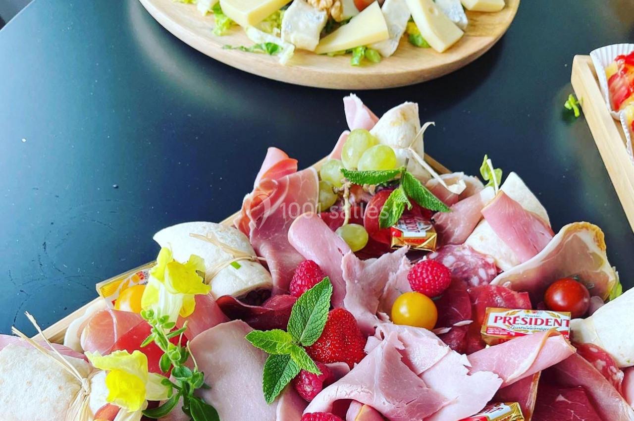 Plateaux garnis de charcuteries, fromages, fruits et légumes frais, présentés sur une table noire.