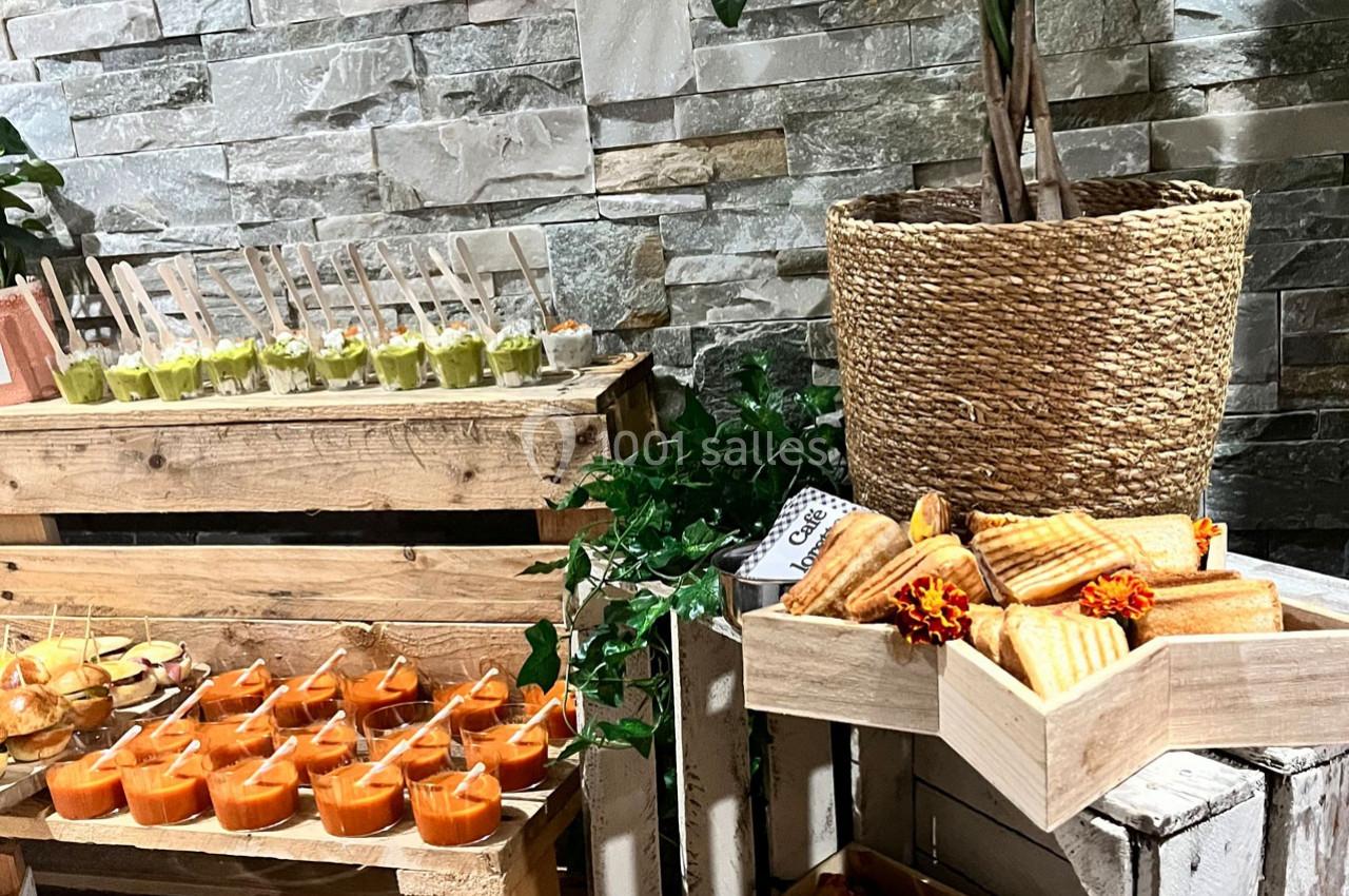 Buffet avec verrines colorées, mini-sandwiches et paninis disposés sur des caisses en bois devant un mur en pierre.
