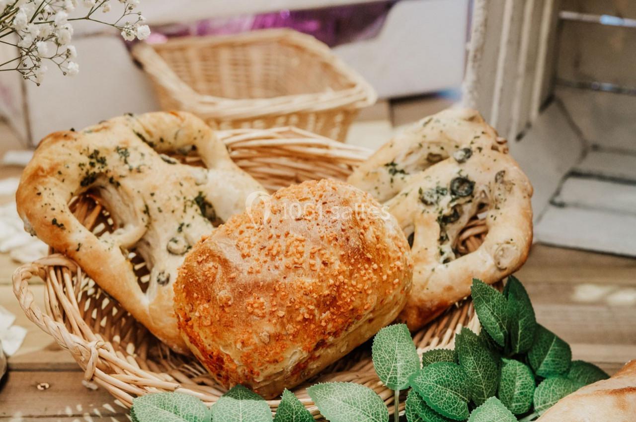 Assortiment de pains artisanaux dans un panier en osier, entouré de feuilles vertes décoratives.