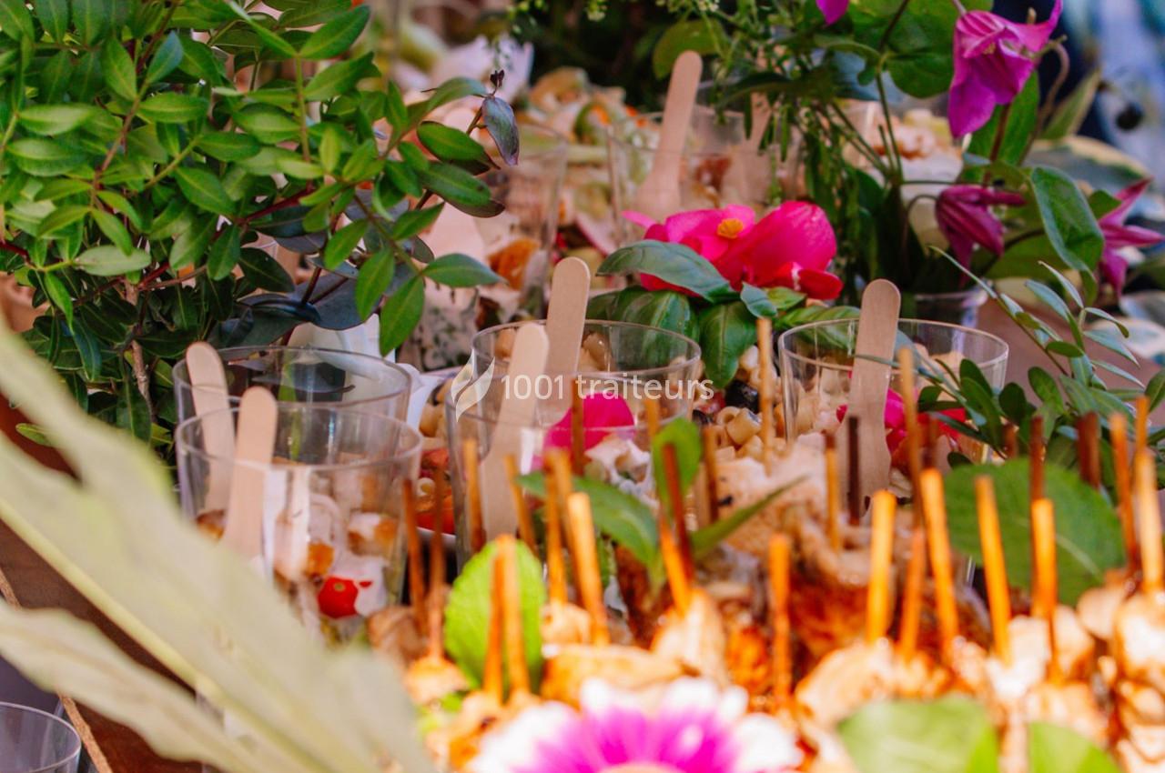 Buffet coloré avec verrines garnies et décorations florales entourées de feuillage vert.