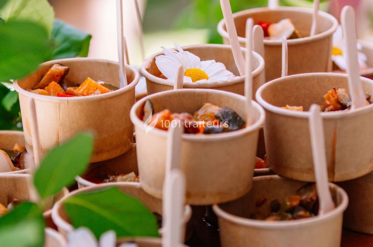 Petits bols en carton remplis de plats colorés, accompagnés de bâtonnets en bois, disposés sur une table avec des fleurs.